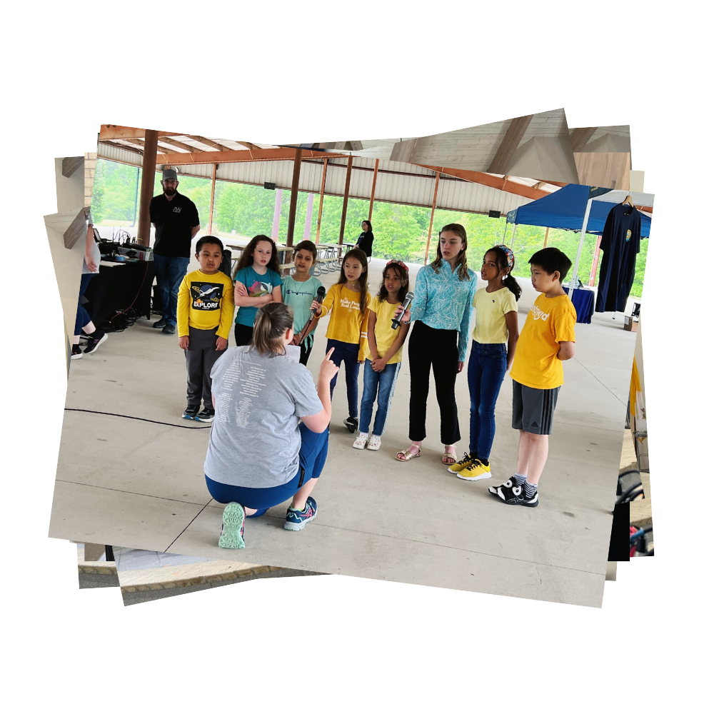 Students in choir sing under pavilion with choir director leading them