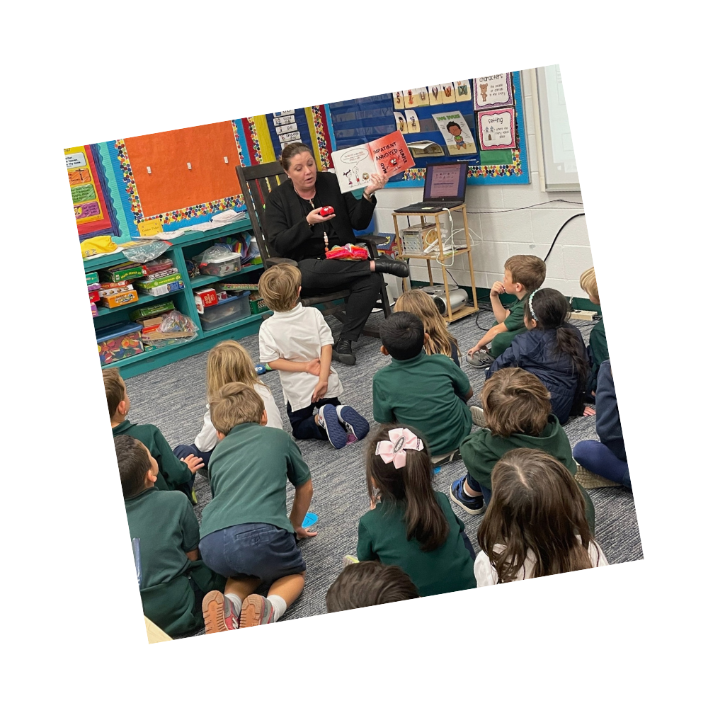 Teacher reads from book and holds toy while students sit on the floor and listen