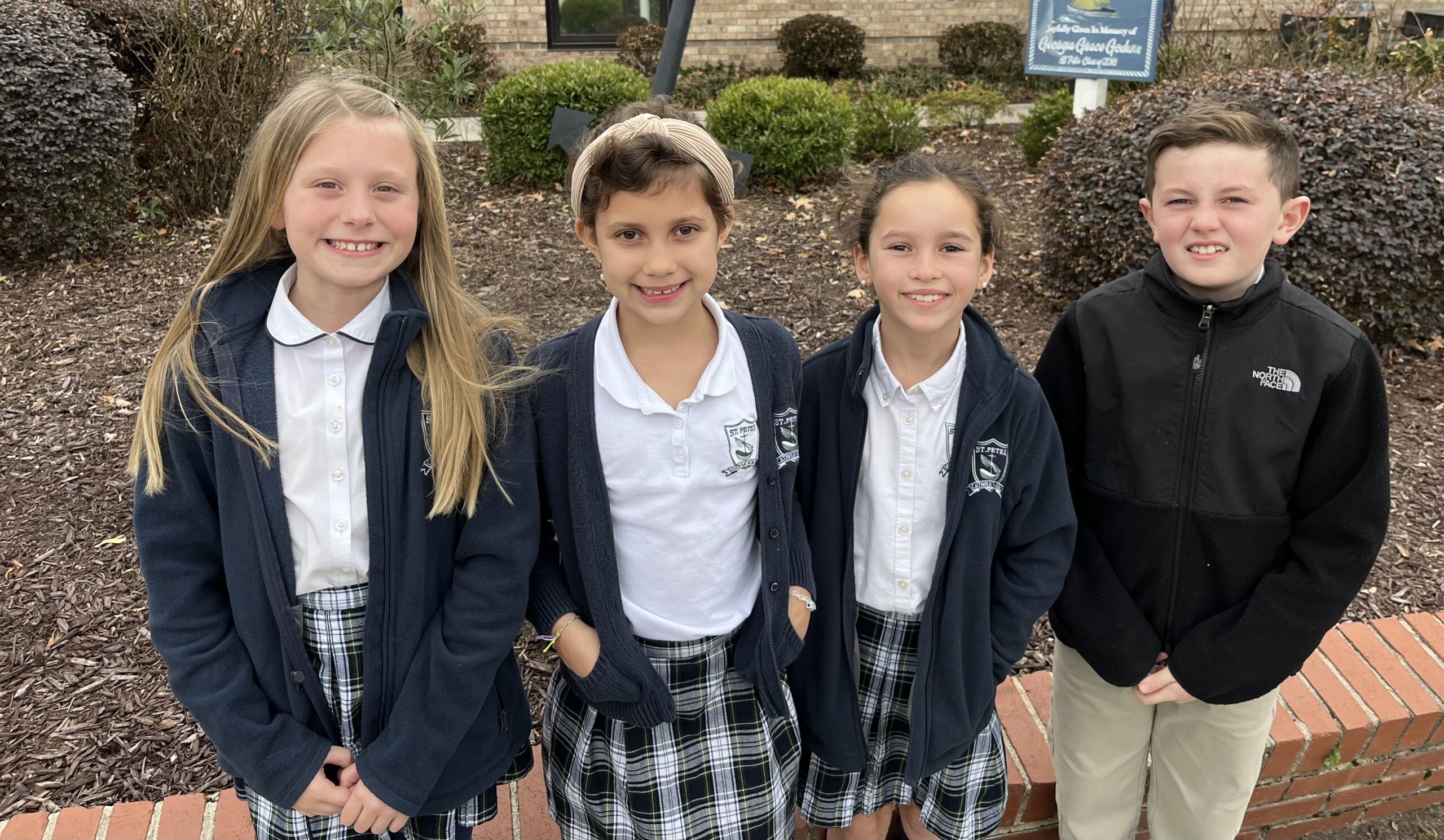 Four elementary students standing outside thechurch dressed in their Saint Peter‘s Catholic school uniforms