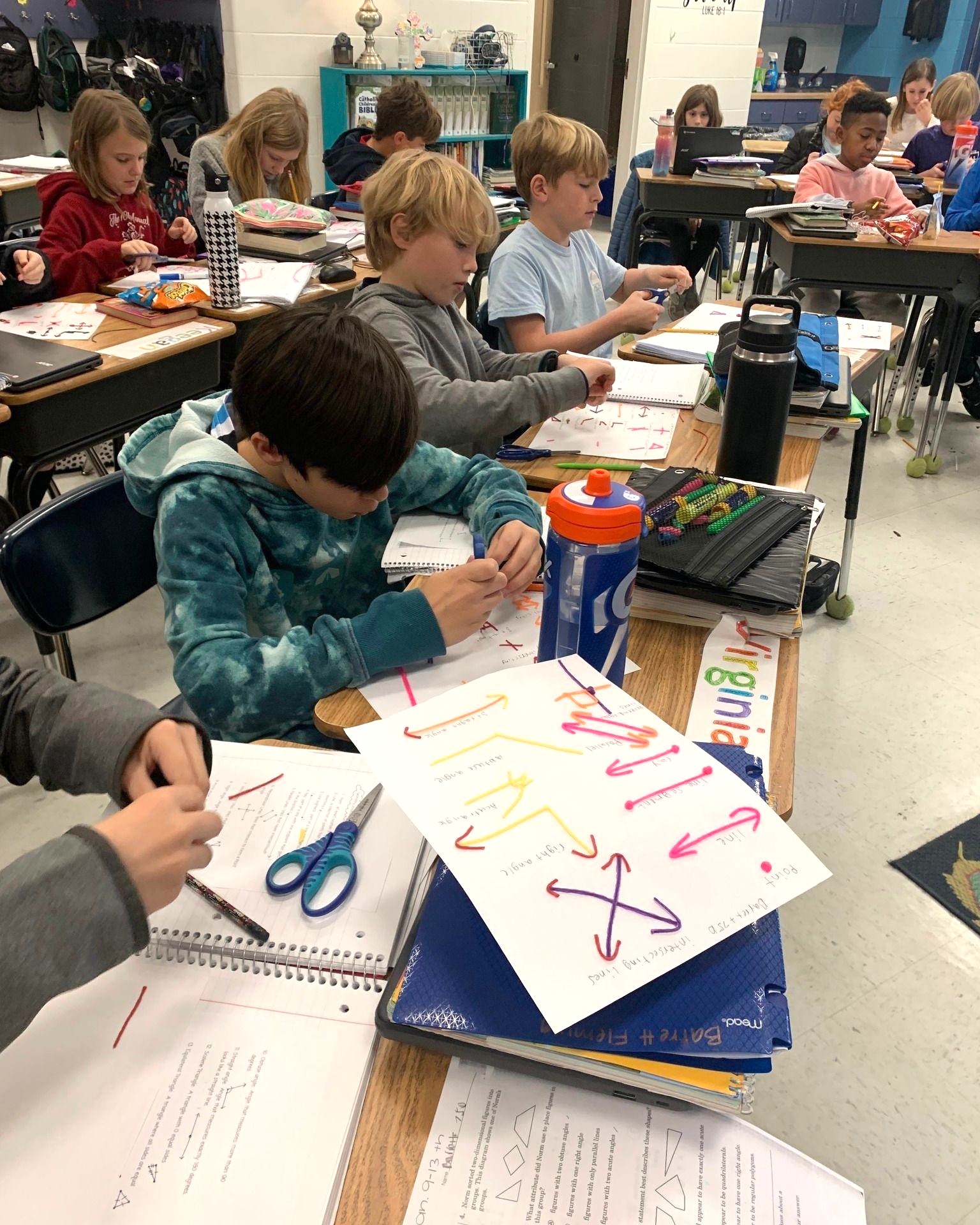 Students work with pipe cleaners at desks to show different types of arrows on paper