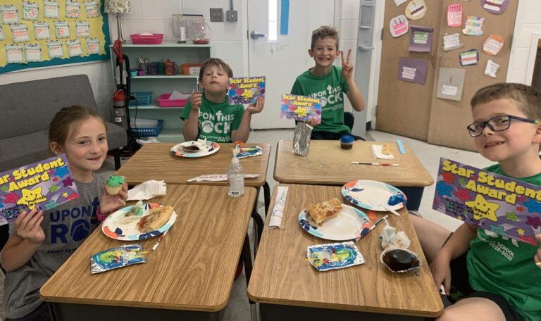 Elementary students pose at the desks, holding their superstar award certificates, for being math superstars