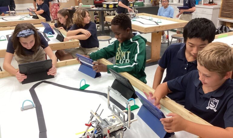 Students at tables coding on iPads with robots on track