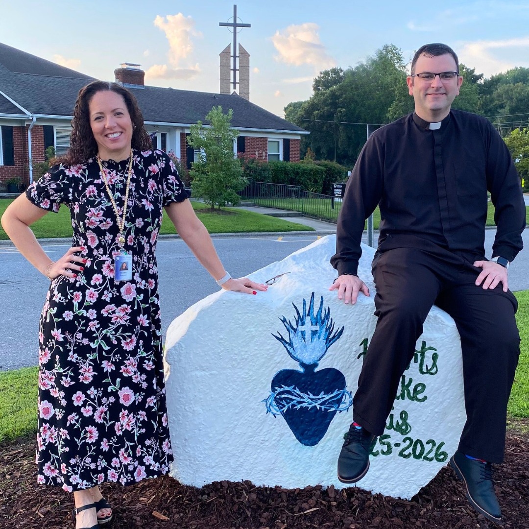 SPCS principal and priest sit on school spirit rock