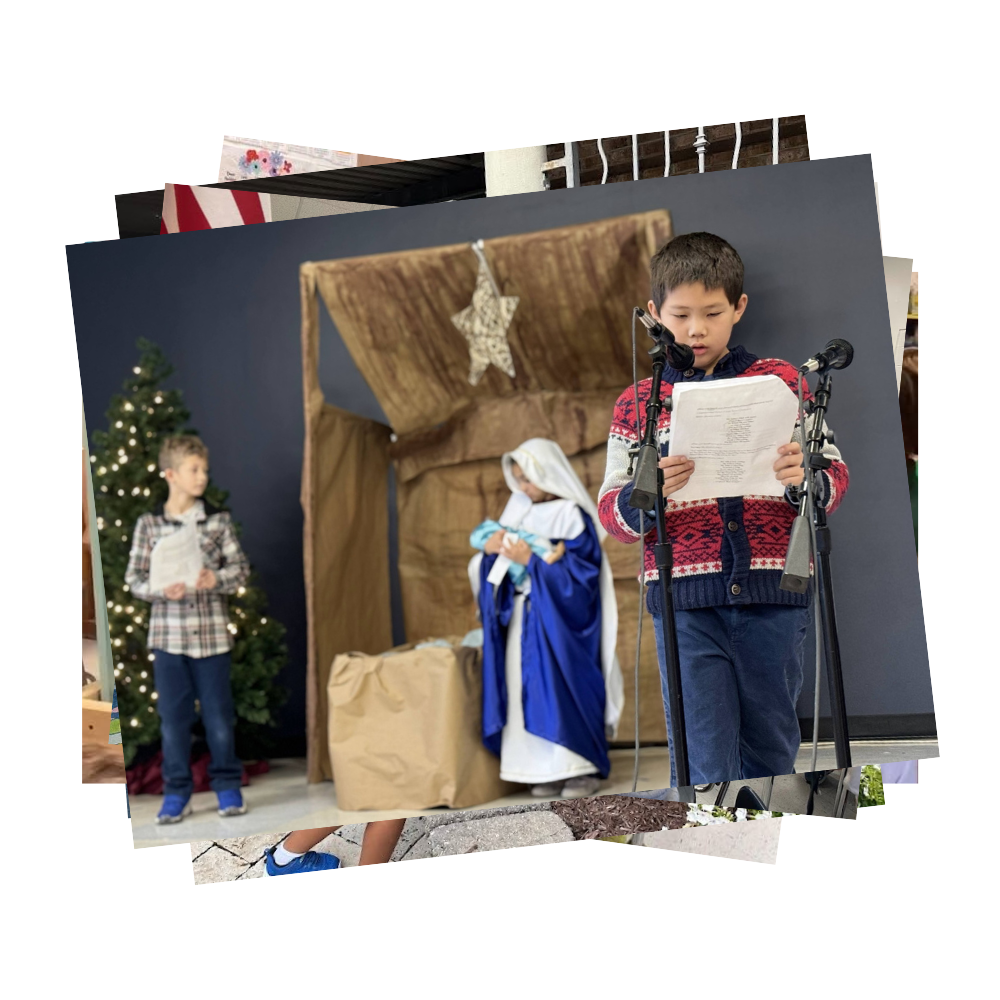 Young boy reading from a paper at a microphone with Nativity play going on in background
