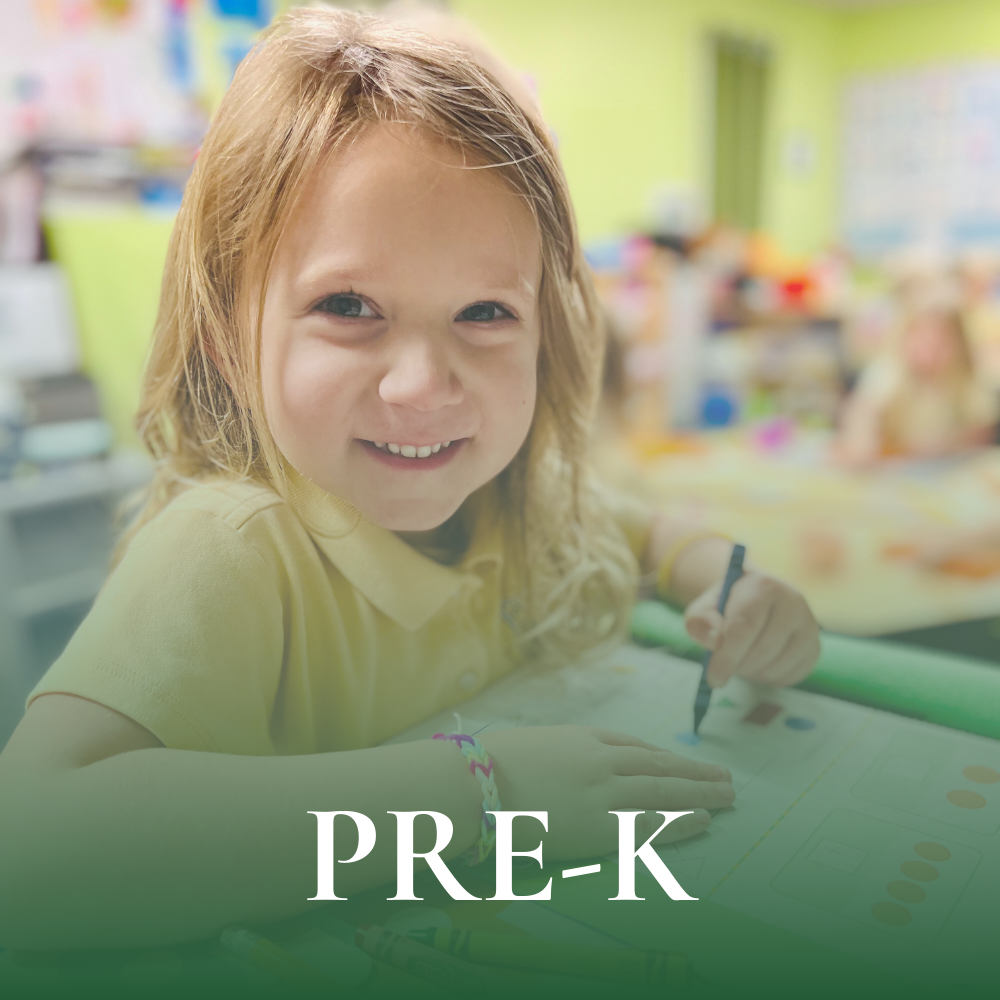 Preschool student sitting at desk smiling and writing in her notebook