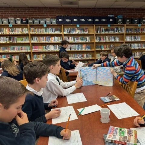 Students reading a table in the library with a book open and worksheets in front of them