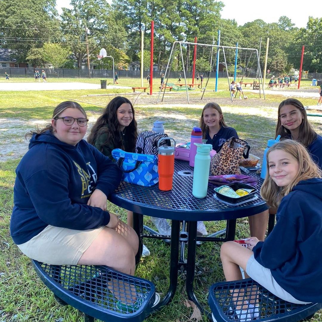 Middle school students eating lunch outside at a picnic table