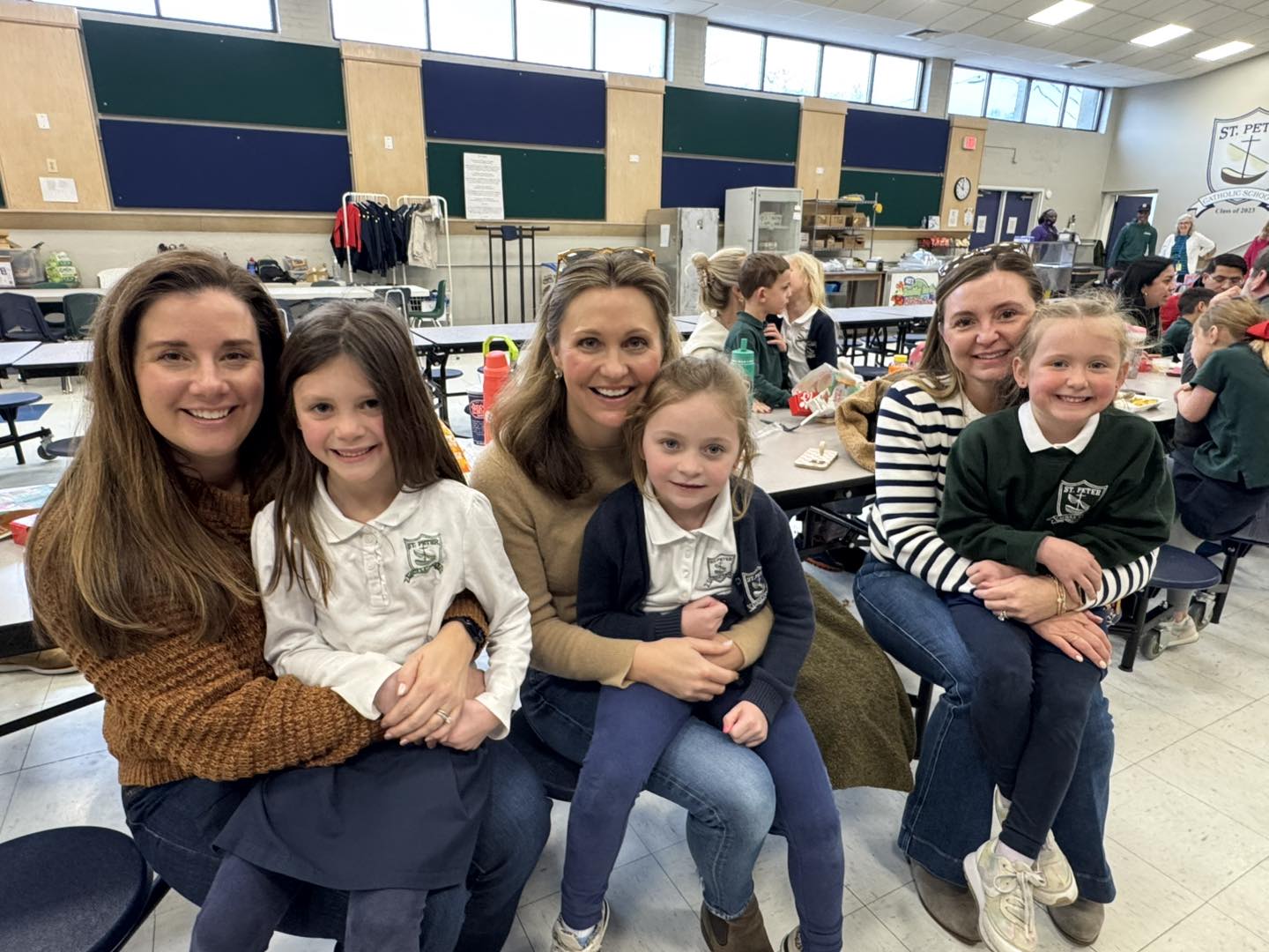 Three Catholic school moms holding their daughters on their laps during school lunch