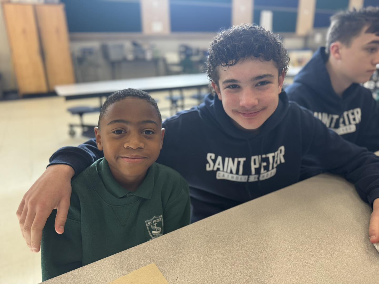 A middle school boy with his arm around a younger student smiling at the camera
