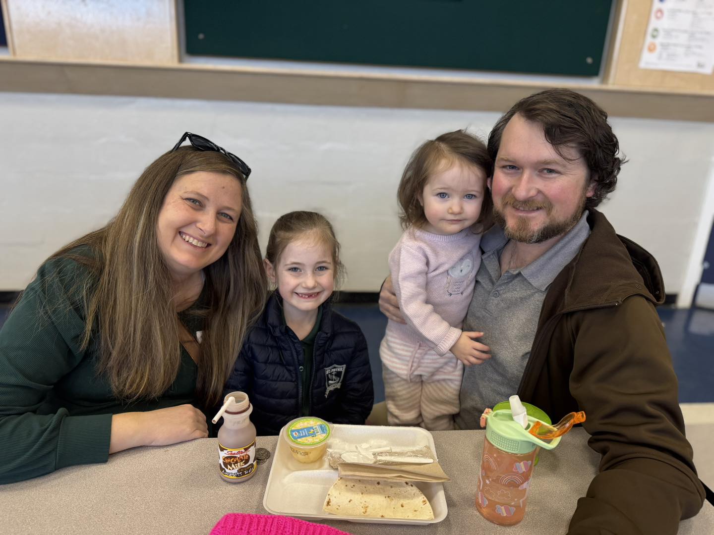 Family smiling at camera while eating lunch at school