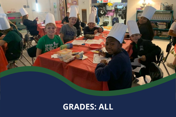 Students wearing chefs hats at a table in a classroom with a caption that reads "Grades: All"