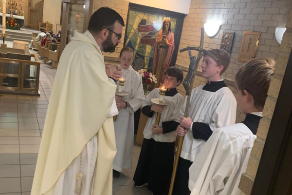 Priest praying with altar servers at the back of church before Mass