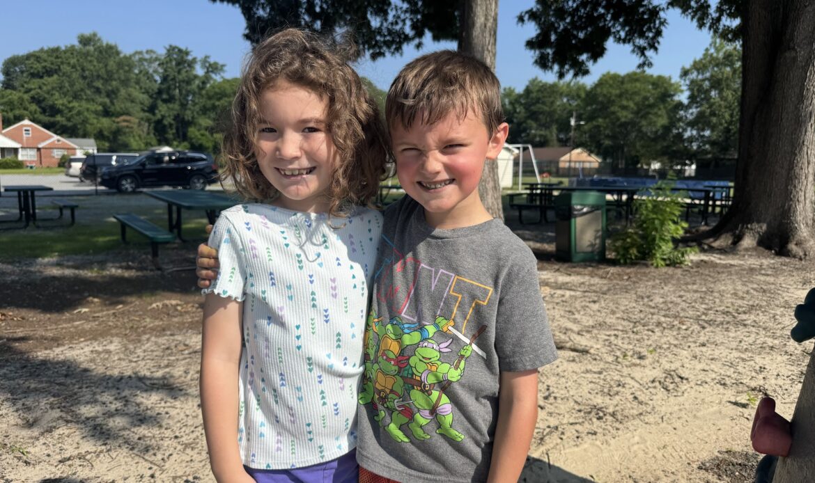 Two kids smiling and looking at the camera on a playground