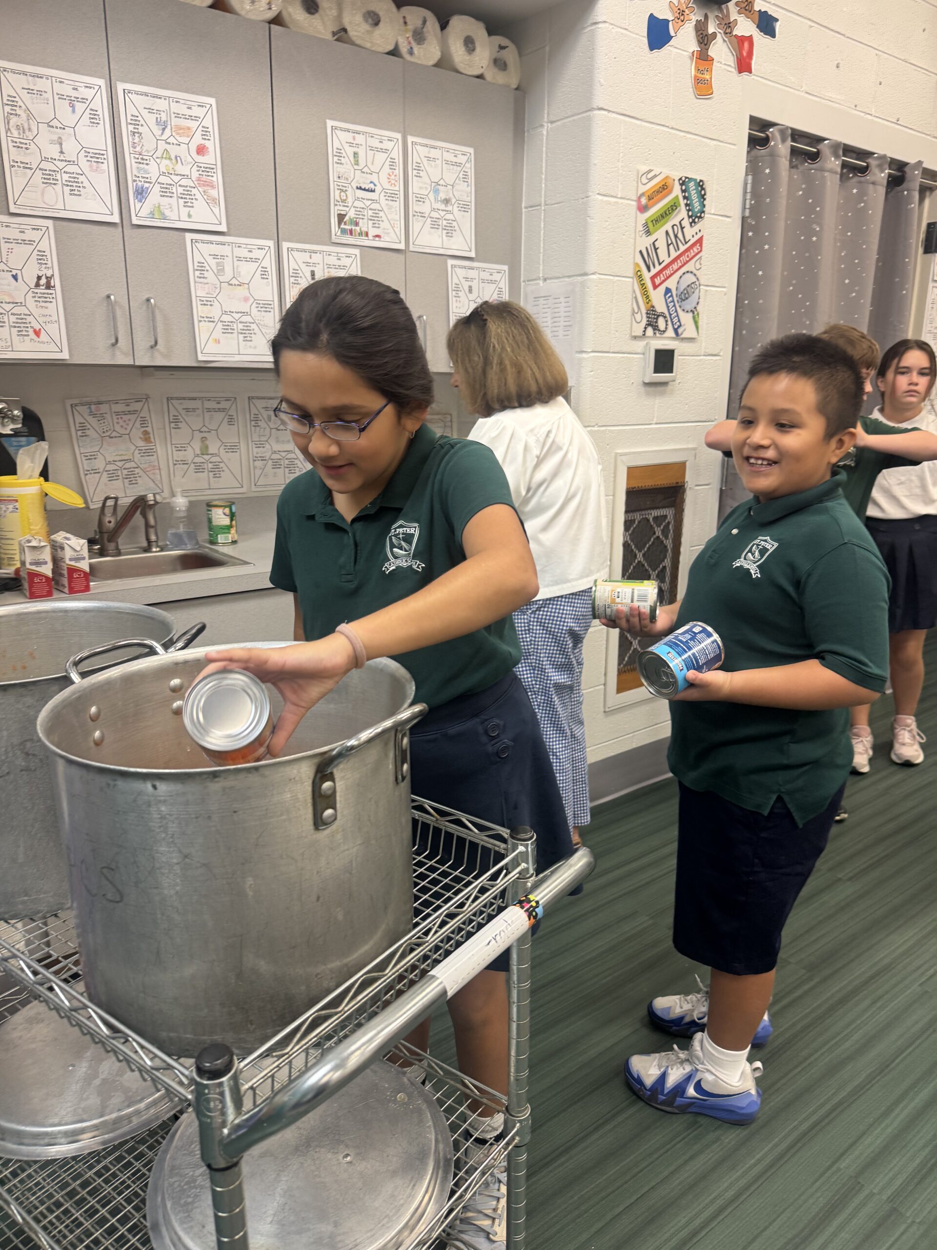 girl pouring can of vegetables into large soup pot while boy smiles at the camera